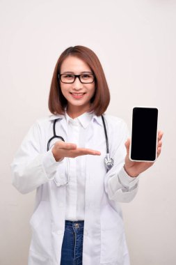  Kadın doktor gülümsüyor ve beyaz arka planda izole edilmiş boş bir akıllı telefon ekranı gösteriyor. 