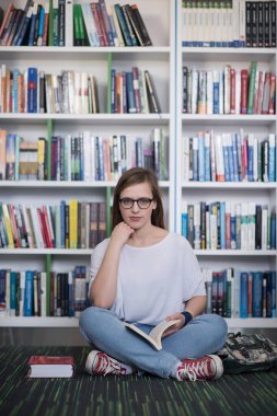 Bayan öğrenci kütüphanede kitap okuyor.