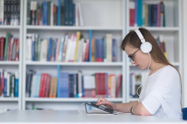 kız öğrenci kütüphanede çalışıyor, tablet kullanıyor ve internetten bilgi arıyor