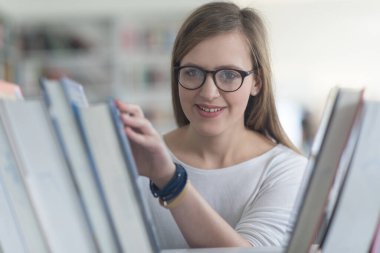 kitaplıkta okumak için kitap seçme kız öğrencinin portresi