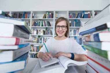 kız öğrenci kütüphanede çalışıyor, tablet kullanıyor ve internetten bilgi arıyor