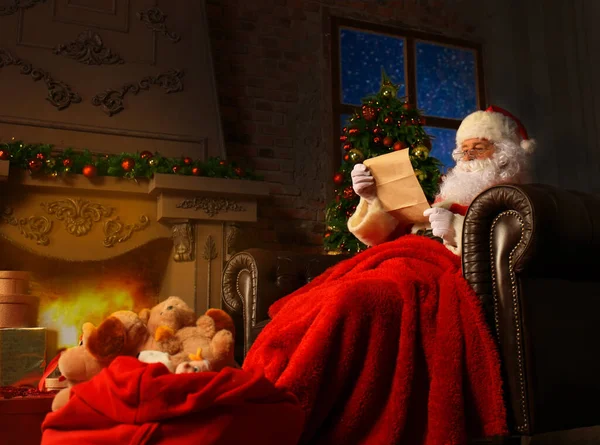 圣诞老人坐在他家靠近圣诞树的房间里看圣诞信或圣诞祝福清单的画像 — 图库照片
