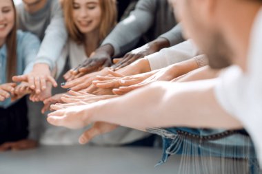 Bir grup gülümseyen genç insan ellerini birleştiriyor.