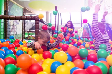 young mom playing with kids in pool with colorful balls clipart