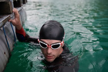 Triatlon sporcusu gölde yüzüyor. Dalış kıyafeti giyiyor.