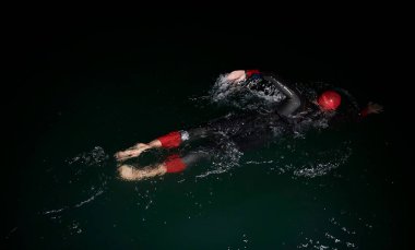 Triatlon atleti karanlık gecede yüzüyor. Dalış kıyafeti giyiyor.