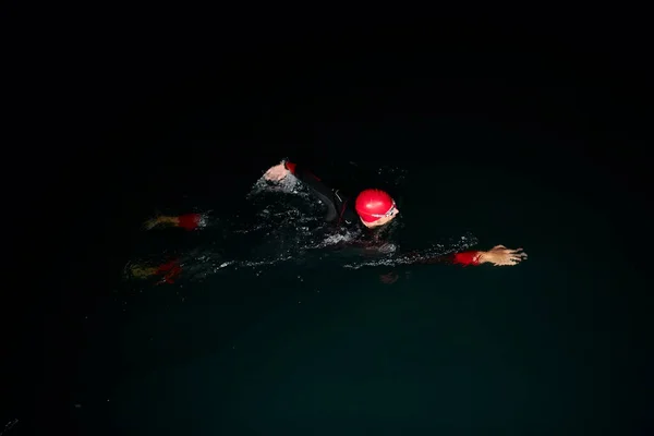 トライアスロン選手がウェットスーツを着て暗闇の中で泳ぐ — ストック写真