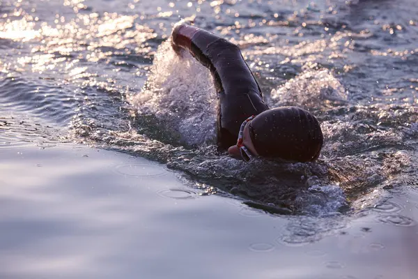 トライアスロン選手がウェットスーツを着て日の出に湖を泳ぎ — ストック写真