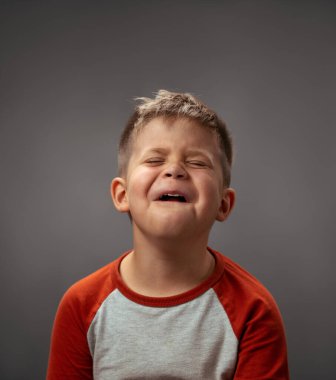Gri arka planda izole edilmiş, ağlıyormuş gibi yapan üzgün bir çocuğun portresi. Sahte duygular. İnsani duygular, yüz ifadesi kavramı. Yüz ifadeleri, duygular, duygular