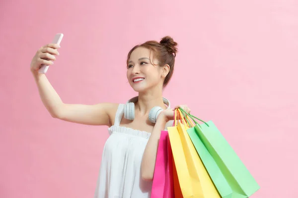 ピンクのバックグラウンドでショッピングバッグをポーズする携帯電話を使用してエキサイティングなアジアのショップアホリック少女 セールス ディスカウントシーズン — ストック写真