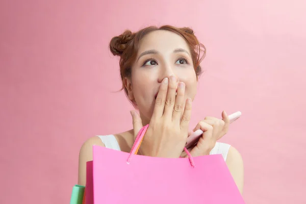 ピンクのバックグラウンドでショッピングバッグをポーズする携帯電話を使用してエキサイティングなアジアのショップアホリック少女 セールス ディスカウントシーズン — ストック写真