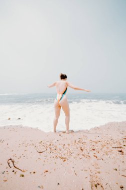 Young lady running and having fun at the beach enjoying warm, tropical ocean water, colorful swimsuit, bright day ocean