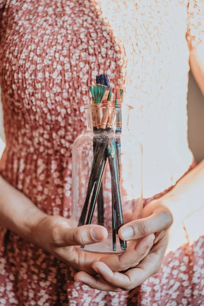 Young woman artist hands grabbing a bottle filled with paint pencils and brushes, ready for painting acrylic. Artistic concepts, artist concept. Beauty dress concept vintage with sun bean
