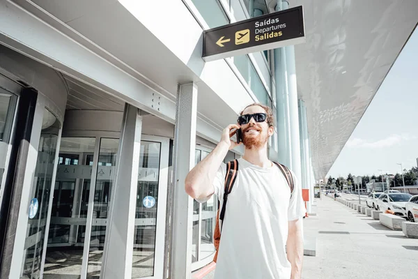 Handsome young hipster man with street clothes talking on phone near airport when arriving at the city,international airport terminal talk on mobile phone book taxi order hotel Air flight trip concept