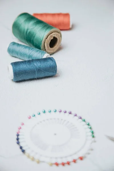 Flat lay composition with sewing accessories: threads, red and gray fabrics, scissors, buttons, set of needles, pins and other sewing tools on a white background. Top view, copy space, mock up.