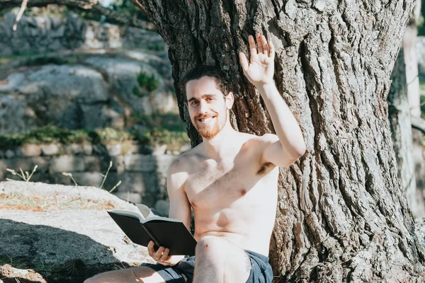 Młody Hipis Spodniach Bez Koszuli Czytający Książkę Drzewie Salutujący Przed — Zdjęcie stockowe