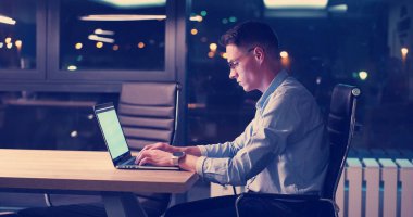 karanlık ofiste dizüstü bilgisayarda çalışan adam