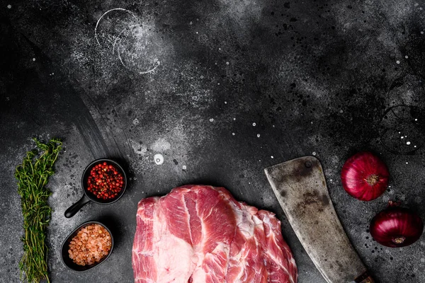Pork shoulder fresh raw meat, with ingredients and herbs , with old butcher cleaver knife, on black dark stone table background, top view flat lay, with copy space for text