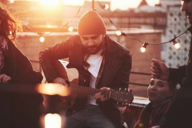 Hava güzel. Arkadaşlar çatı katındaki partide dekoratif renkli ampullerle eğleniyor.