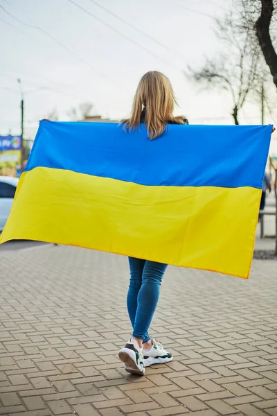 Portrait of a joyful Ukrainian woman holding a Ukrainian flag and a sign. The girl is waiting for her husband from the war. War between Russia and Ukraine.