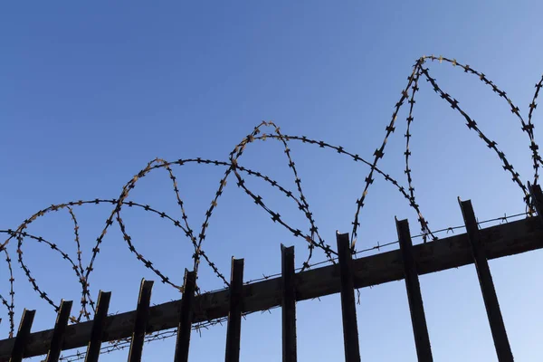 青い空に対する高い金属製の柵の上に鉄条網 — ストック写真