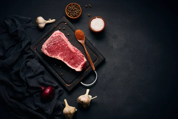 骨の上に生のジューシーな牛肉肉は 木製のまな板の上にあり 黒い背景で調理するためのスパイスです Tenderroin New York — ストック写真