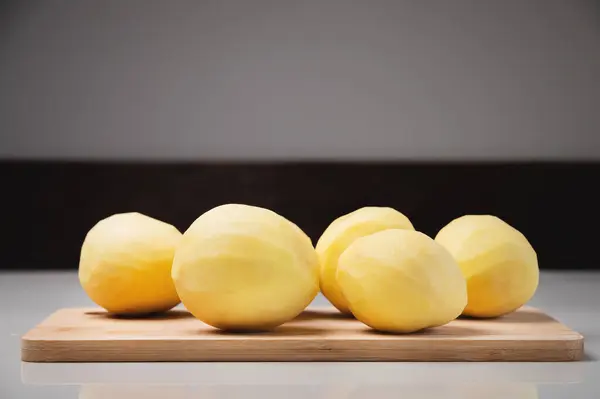 Beyaz Bir Masanın Üzerindeki Tahta Kesme Tahtasının Üzerinde Soyulmuş Patatesler — Stok fotoğraf