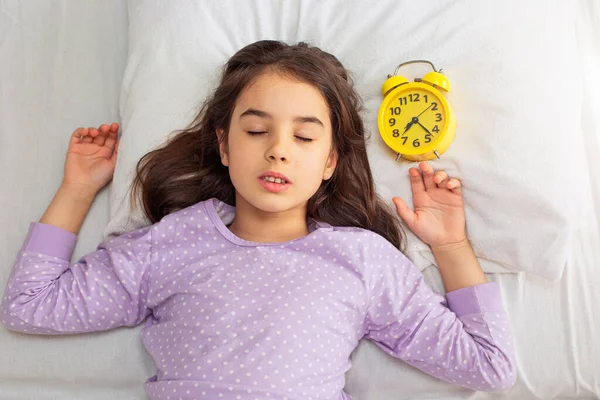Χαριτωμένο Μελαχρινό Κορίτσι Κοιμάται Ένα Κίτρινο Ξυπνητήρι Ένα Λευκό Μαξιλάρι — Φωτογραφία Αρχείου