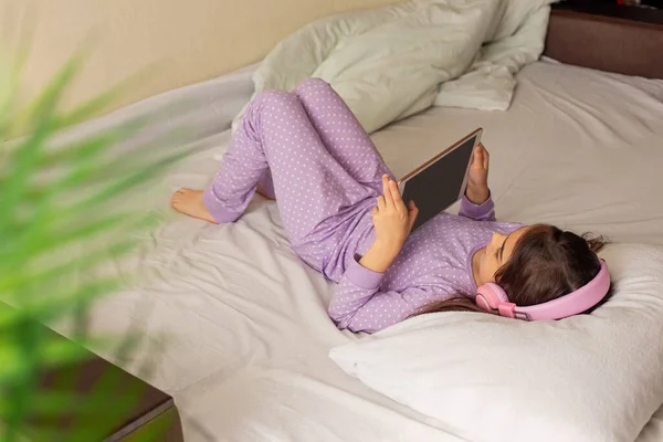 Tyttö Violetissa Pyjamassa Makaa Valkoisella Sängyllä Selässään Pitää Vaaleanpunaista Digitaalista — kuvapankkivalokuva
