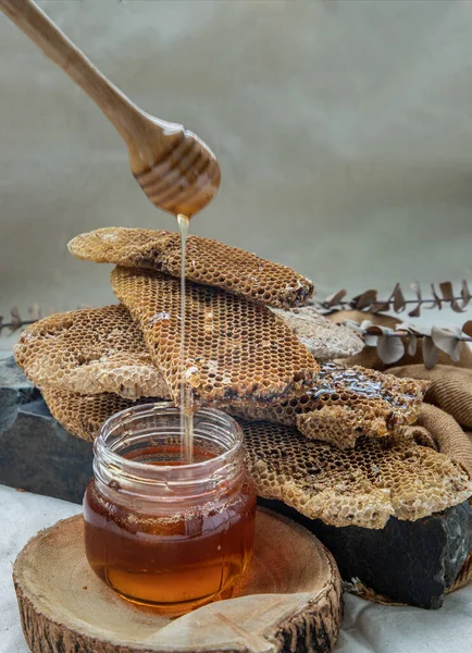 美味的蜂蜜滴在玻璃瓶和新鲜蜂窝的背景上 — 图库照片