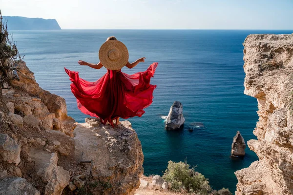 一个穿着飘扬的红色连衣裙的女人在风中飘扬 戴着草帽在大海的衬托下飘扬 — 图库照片