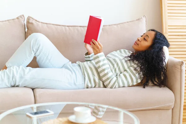 Αφρο Αμερικανός Ξαπλωμένος Στον Καναπέ Και Διαβάζοντας Βιβλίο Κόκκινο Εξώφυλλο — Φωτογραφία Αρχείου