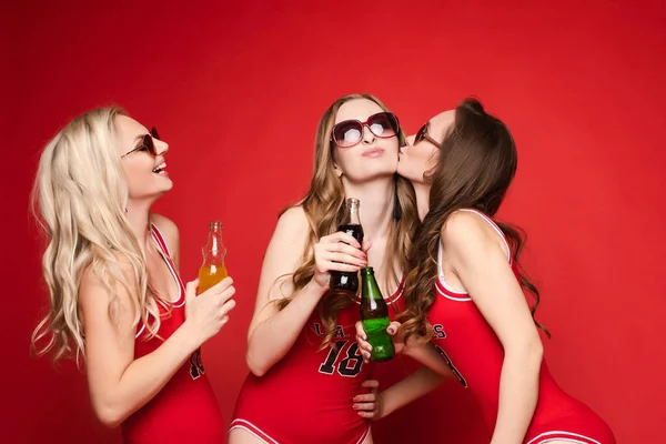 美しく幸せな女性の友人で明るい赤水着で冷たい飲み物で彼らの手に赤の背景に スタジオ — ストック写真