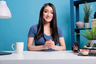 Masada oturmuş kameraya gülümseyen Asyalı vlogger portresi