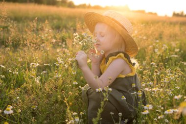 Bir buket papatyayla tarlada hasır şapkalı küçük sarışın kız.