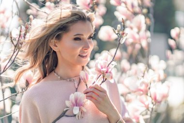 Portrait of a beautiful happy middle aged woman enjoying the smell in a blooming spring garden. Beautiful magnolia bushes, large flowers.