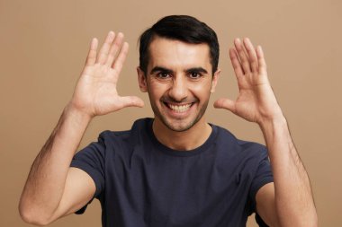 Gri tişörtlü yakışıklı adam, el hareketi, gülümse, duygular bej arka plan.