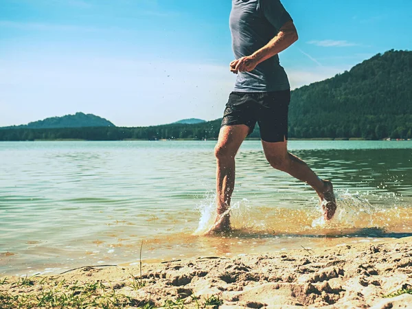 裸足のスポーツマンが砂浜に沿って水の中を走る — ストック写真