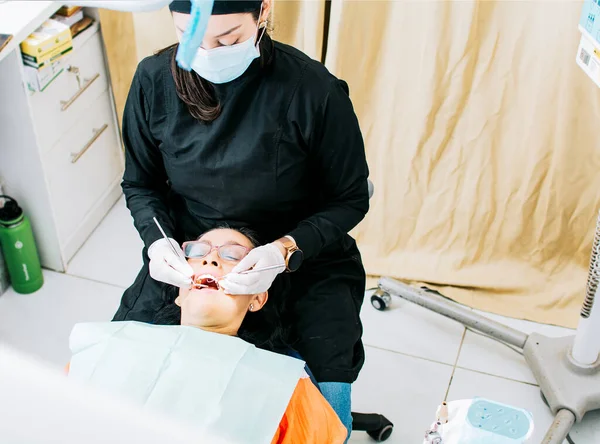 女性の患者に歯科を行う女性歯科医患者が横になって歯科医師は 患者に口を検査歯科医師は 胃学を実行 — ストック写真