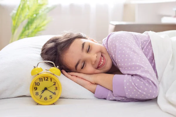 보라색 파자마를 사랑스럽게 미소짓는 소녀가 침대에 베개를 — 스톡 사진