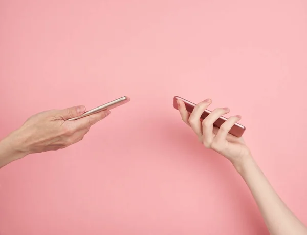 Two women hold phone on pastel pink background copy space side view