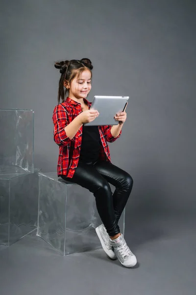 Kleines Mädchen Sitzt Blockhaft Und Sieht Digitales Tablet Vor Grauem — Stockfoto