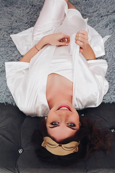 美しいです幸せな女の子で白い絹のローブと睡眠マスクオンベッド — ストック写真