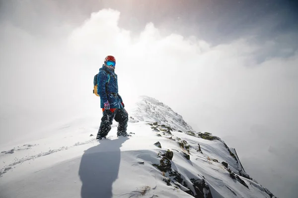 一个穿着滑雪服站在山顶上 用背挡住太阳的人的画像 — 图库照片