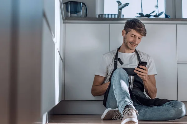 Jovem Com Smartphone Sentado Chão Cozinha — Fotografia de Stock