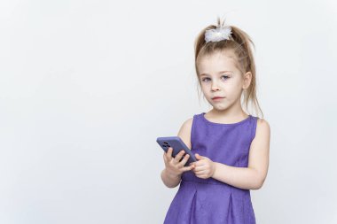 Stüdyoda akıllı telefonuyla poz veren mavi elbiseli 5-6 yaşlarında tatlı bir kız.