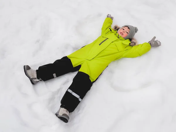 Yeşil Tulumlu Gülümseyen Çocuk Karda Kar Meleğini Şekillendiriyor Karlı Havada — Stok fotoğraf