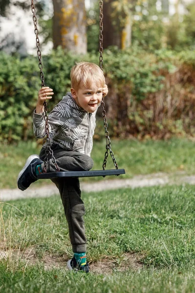 这个金发碧眼的男孩试图在没有父母帮助的情况下爬上铁链时玩着秋千 — 图库照片
