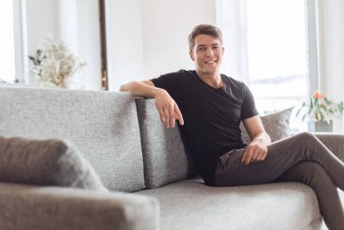 Düşünceli genç adam oturma odasında kanepede oturuyor..