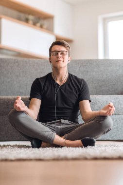 Lotus pozisyonunda oturan sıradan bir adam oturma odasında halının üzerinde oturuyor.
